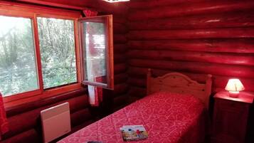 Een slaapkamer in een blokhut met een enkel bed, een raam, een heater en een nachtkastje met een lamp.