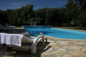 A swimming pool with lounge chairs and a glass of orange juice.