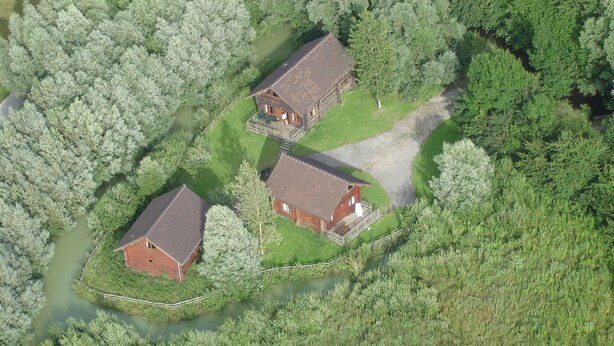 Two wooden cabins surrounded by dense forest, with a small stream nearby. - Chalet in France Near the Beach & Pool (Quend)