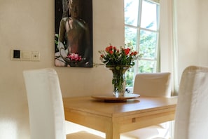 Una mesa de comedor con sillas, un jarrón con flores, un cuadro en la pared y una ventana con luz natural.
