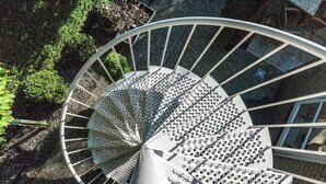 En spiraltrappa med metallräcken och en cirkelformad design, omgiven av grönska.