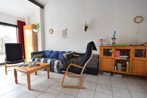 A living room with a sofa, a chair, a wooden cabinet, and a window. - Great Holiday Home Near a Pleasure Marina, the Mediterranean and the Pyrenees (Saint-Cyprien)