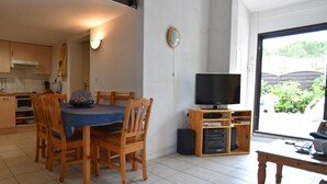 A dining area with a table and chairs, a television, and a kitchen in the background. - Great Holiday Home Near a Pleasure Marina, the Mediterranean and the Pyrenees (Saint-Cyprien)