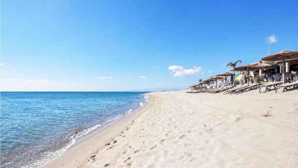 A beach with a clear sky, a sandy shore, and a row of beachside structures with umbrellas. - Great Holiday Home Near a Pleasure Marina, the Mediterranean and the Pyrenees (Saint-Cyprien)