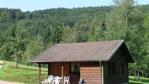 A wooden cabin with a porch, outdoor seating, and a view of a forested hillside. - Ventron Chalet With Hill Views (Ventron)