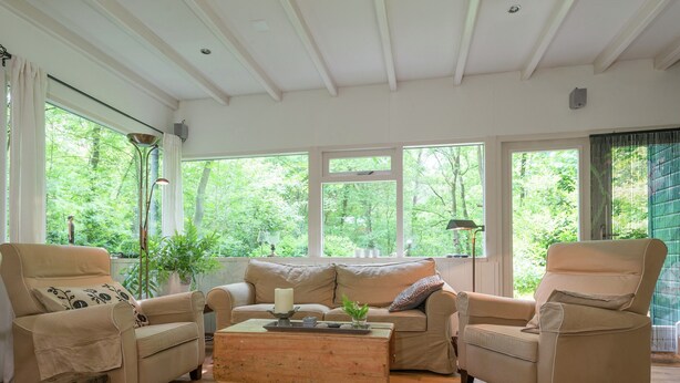 A cozy living room with a beige sofa set, a wooden coffee table, and large windows offering a view of greenery outside. - Cozy Countryside Escape in Dalfsen (Dalfsen)