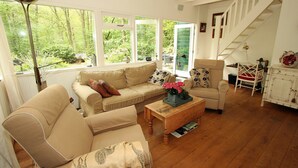 A spacious living room with a sofa, armchair, and a coffee table. There is a staircase leading to another level, and large windows providing a view of the outdoors. - Cozy Countryside Escape in Dalfsen (Dalfsen)