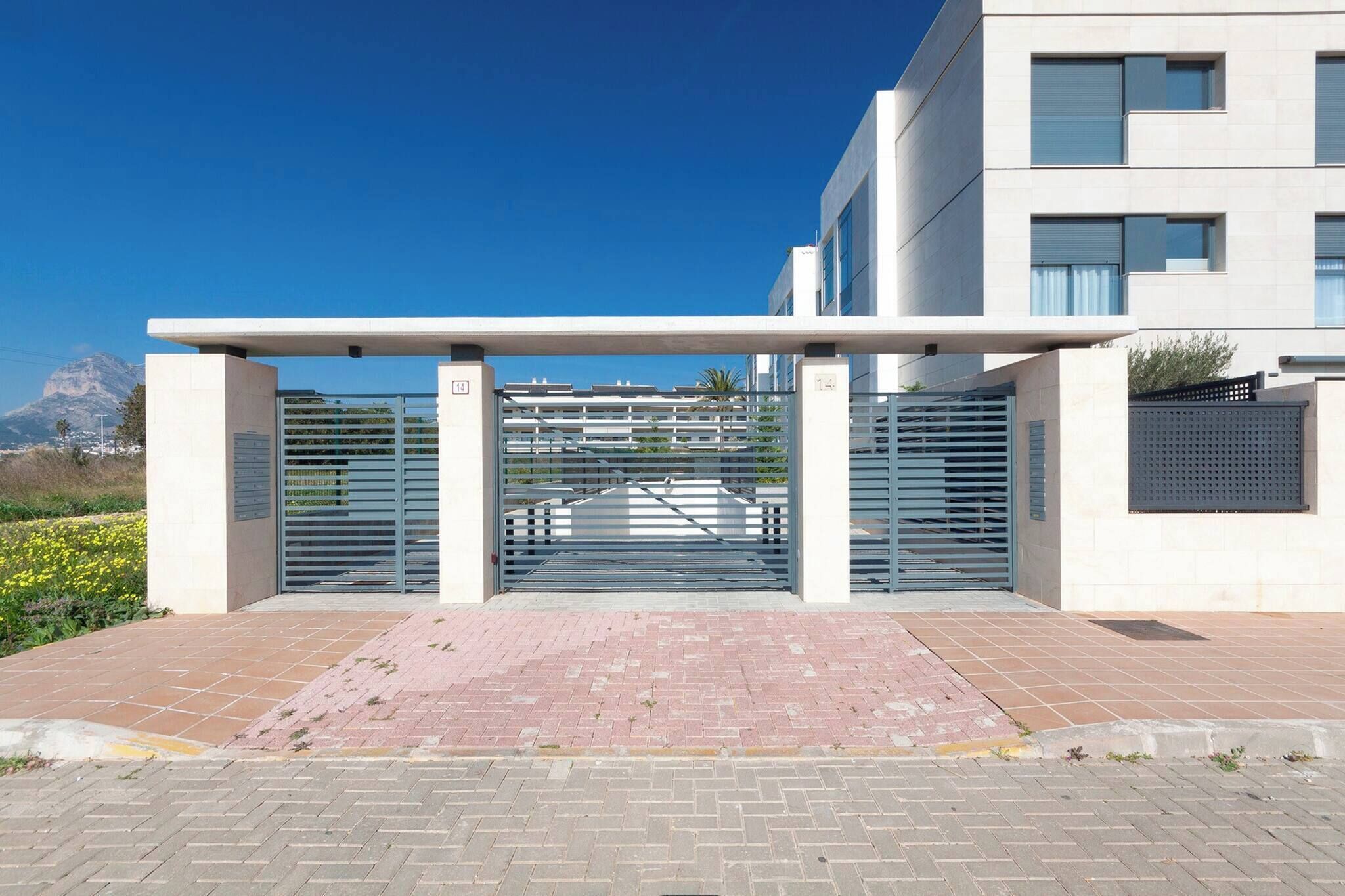 A modern building with a gated entrance, a paved pathway, and a mountain in the background.