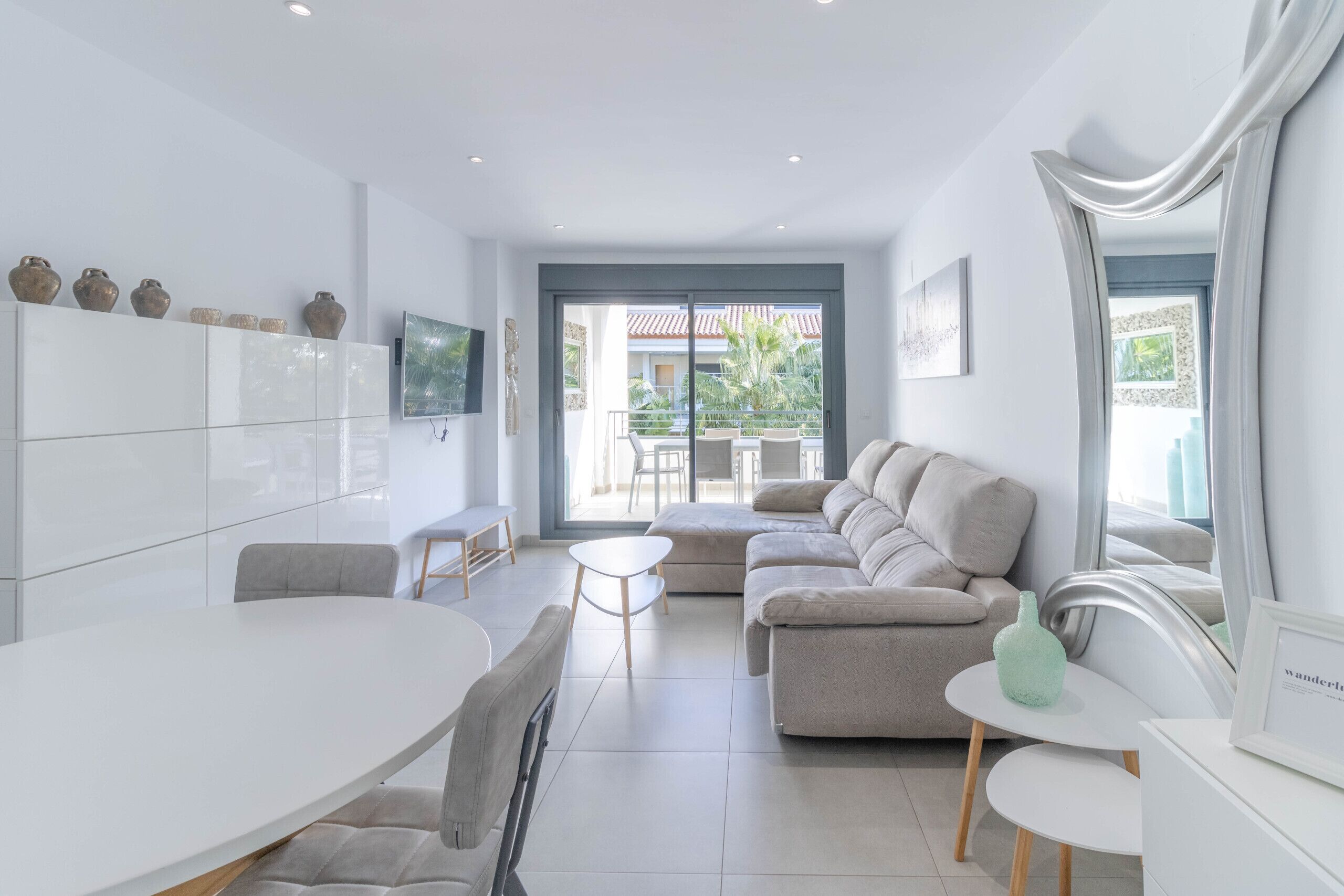 A modern living room with a white sofa, a dining table, and a large window.