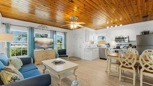 A spacious living area with a wooden ceiling, a dining table with chairs, a sofa, and a TV. - 30ft from Perfect LAGUNA BEACH ~ Directly across the street from Beach Access #83 "Oleander West Cottage" (Panama City Beach)
