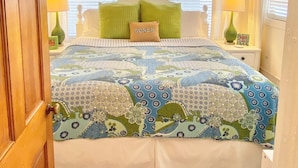 A bedroom with a wooden ceiling, a bed with a patterned quilt, green pillows, and a ceiling fan. - 30ft from Perfect LAGUNA BEACH ~ Directly across the street from Beach Access #83 "Oleander West Cottage" (Panama City Beach)