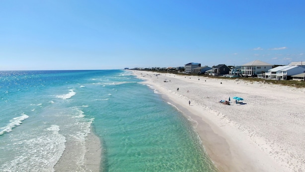 A beach with clear turquoise water, sandy shore, and buildings in the background. - 30ft from Perfect LAGUNA BEACH ~ Directly across the street from Beach Access #83 "Oleander West Cottage" (Panama City Beach)