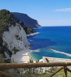 A coastal landscape with a beach, cliffs, and a clear blue sea.