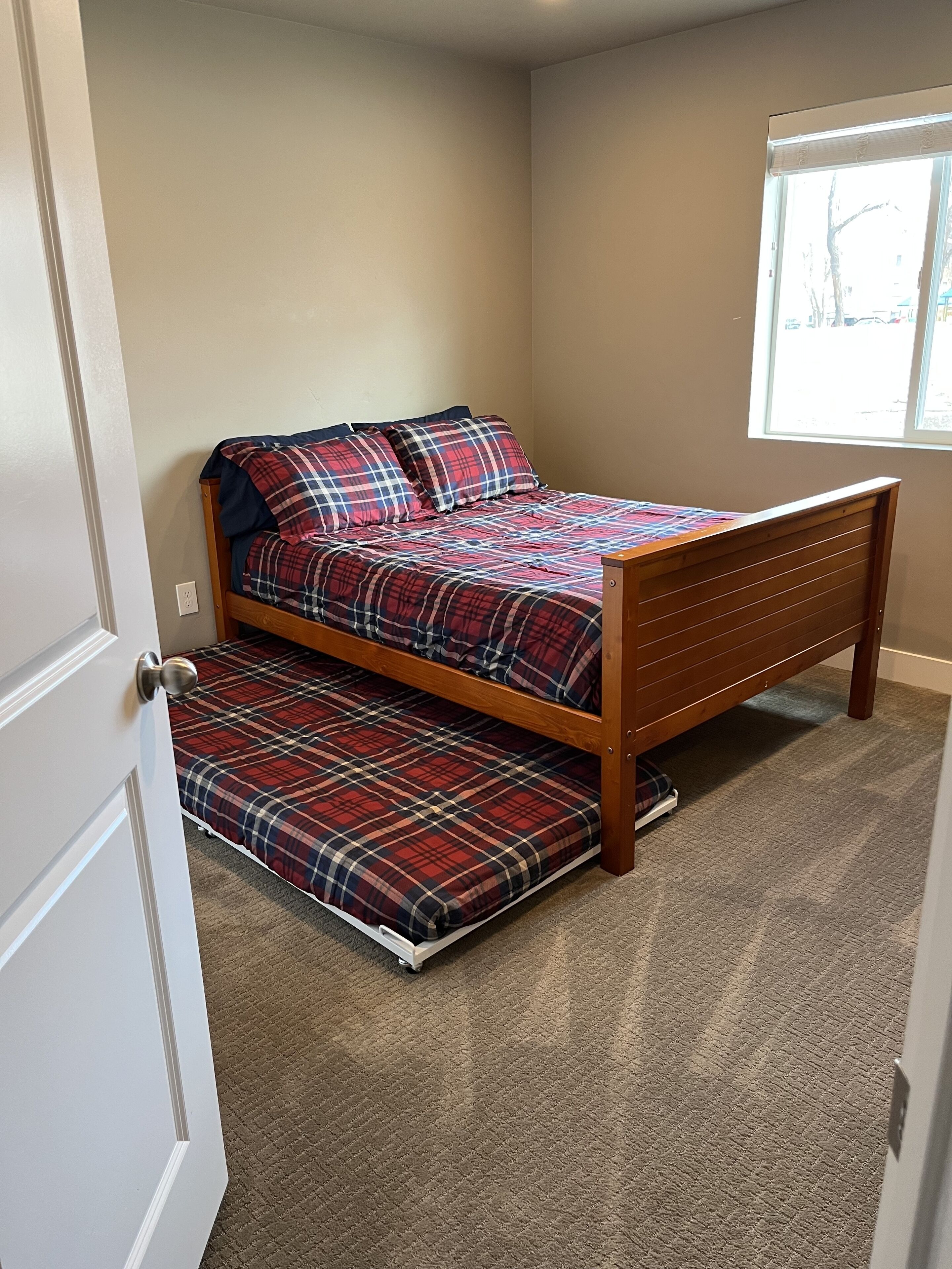 Ein kleines Zimmer mit einem Einzelbett, Holzrahmen, Karomuster-Bettwäsche und Teppichboden.