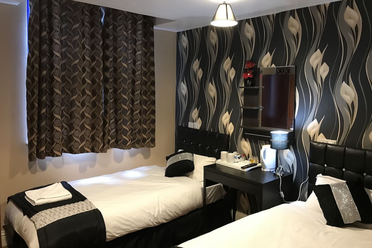 Habitación de hotel con dos camas, un escritorio con lámpara, un espejo y una pared decorativa con diseño de hojas.