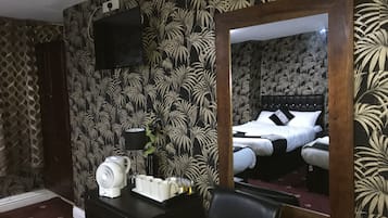 A hotel room with a large mirror reflecting a bed, a TV mounted on the wall, a desk with a fan, and a coffee maker.