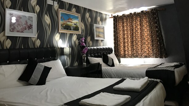 Ett hotellrum med två sängar, ett nattduksbord, en lampa och ett fönster med gardiner.