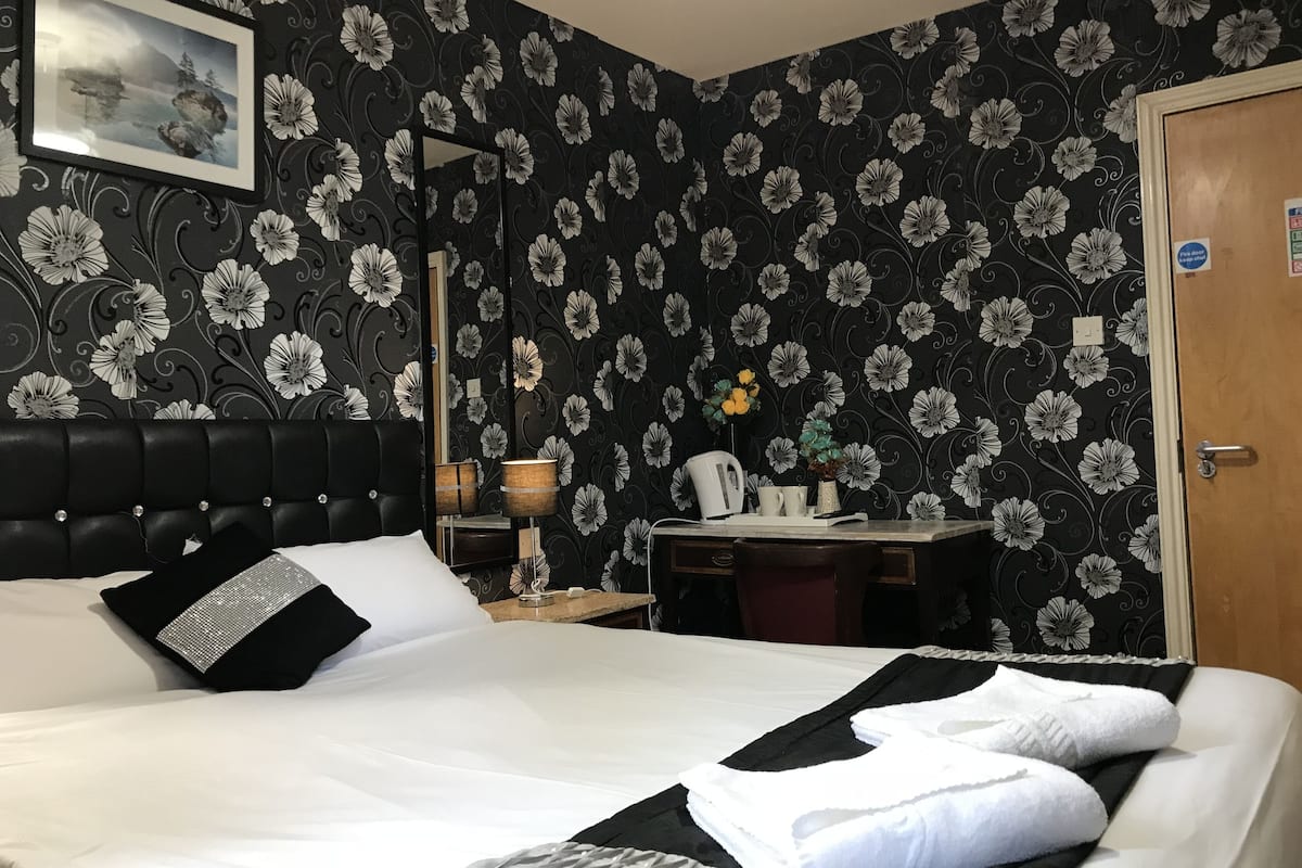 Una cama bien tendida con ropa de cama blanca y negra, un cabecero negro y un estampado de papel tapiz floral.