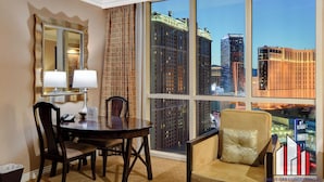 A hotel room with a large window offering a city view, a dining table with chairs, a sofa, and a mirror with a lamp. - MGM Signature-F1 Track View Near Strip Lazy River (Las Vegas)