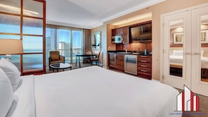 A hotel room with a large bed, a desk, a chair, a kitchenette, and a view of the city. - MGM Signature-F1 Track View Near Strip Lazy River (Las Vegas)