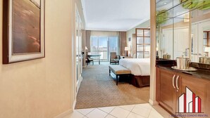 A hotel room with a bed, a desk, a chair, a large window, and a view of the city.