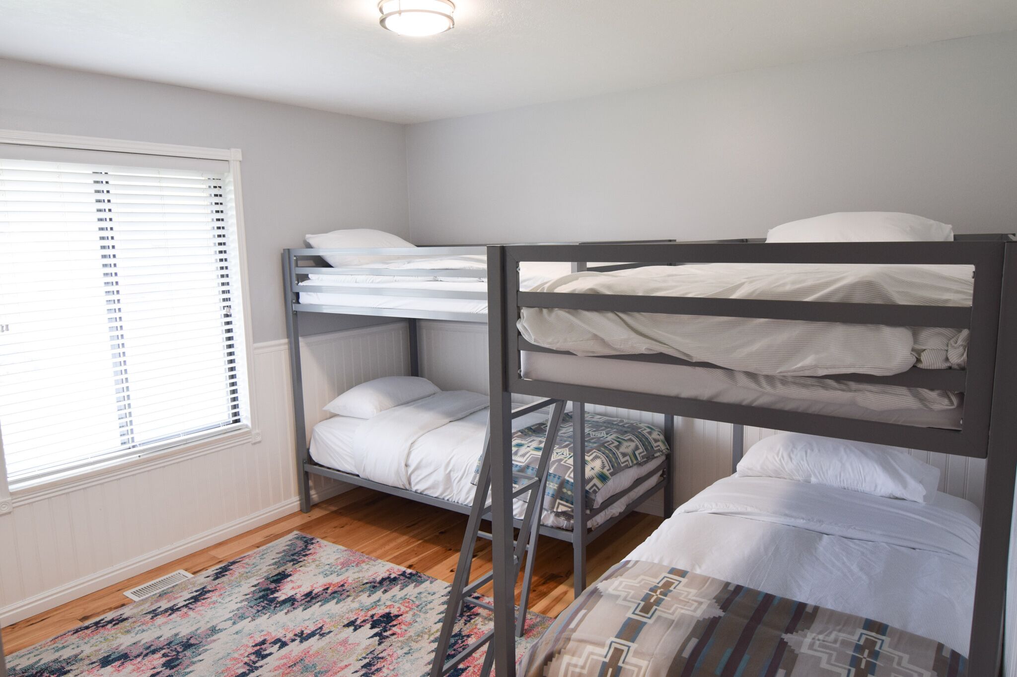A bunk bed room with a window, a patterned rug, and a ceiling light.
