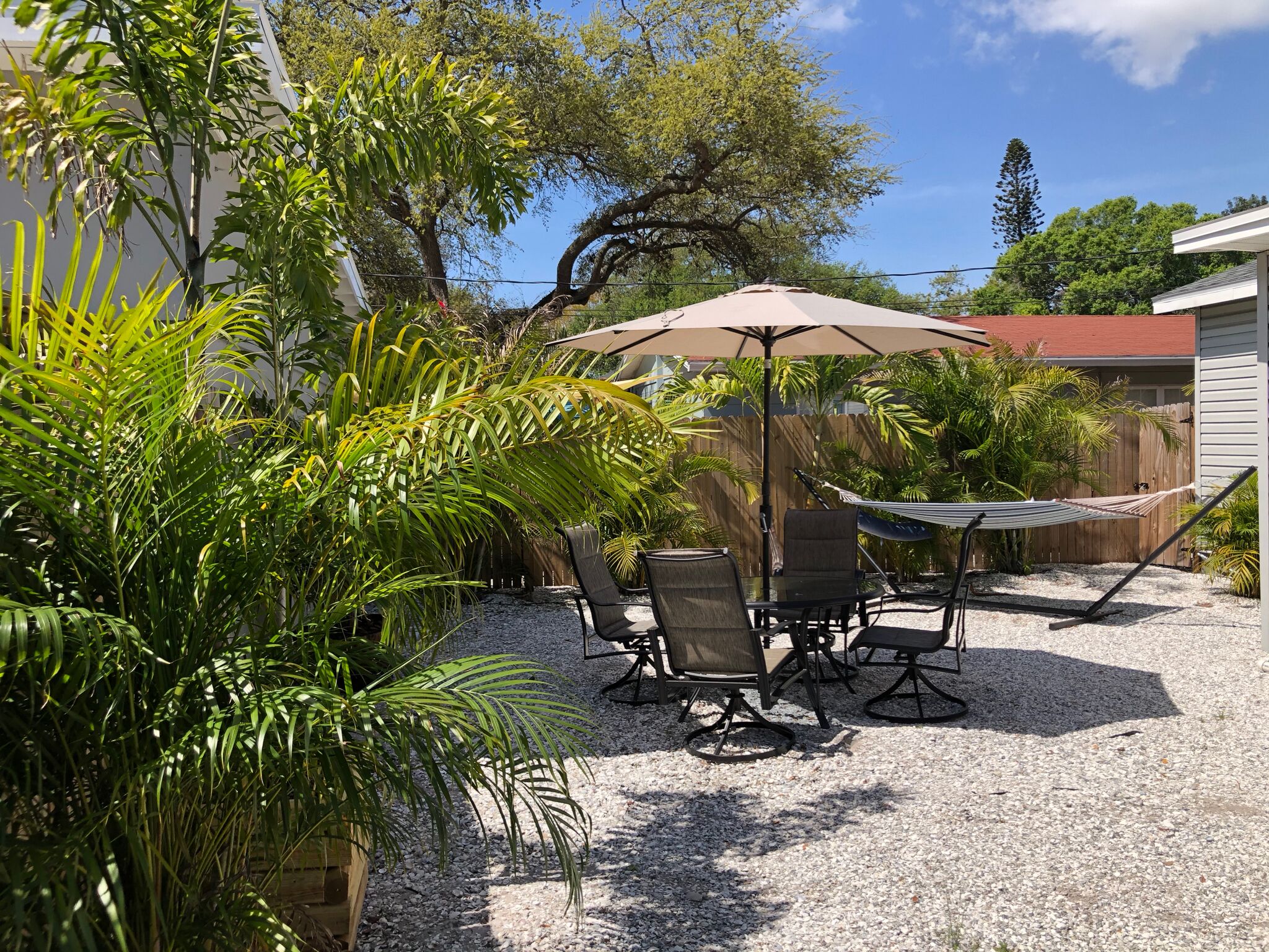 Un patio exterior con una mesa, sillas, una hamaca y un paraguas grande.