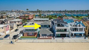 Un quartier résidentiel situé sur la côte, composé d’un mélange de maisons à un ou plusieurs étages, avec une marina en arrière-plan et une plage de sable au premier plan.