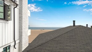 Un bâtiment à l’extérieur blanc et au toit gris, qui surplombe une plage sous un ciel dégagé.