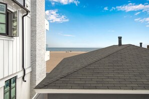 A building with a white exterior and a grey roof, overlooking a beach with a clear sky.