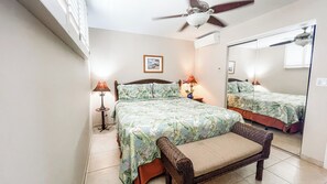 Una camera da letto con due letti, un ventilatore a soffitto, un comodino con lampade, una sedia in vimini e uno specchio.