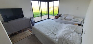 Relax in a spacious bedroom with a large bed, flat-screen TV, and seating area, offering a balcony with a view of a lush green area.