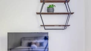 Moderni olohuone, jossa on televisio puisen jalustan päällä, sohva ja geometrisesti muotoiltu seinähylly, jossa on kasvi.