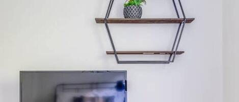 A modern living room with a TV on a wooden stand, a sofa, and a geometric wall shelf with a plant.