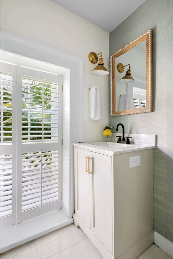 A bathroom with a white vanity, a large mirror, and a window with white blinds.