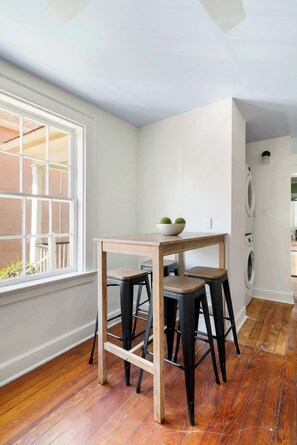 A corner kitchen with a wooden table, stools, and a window with a view of the outside. - High Society | Historic District Gem Near King St (Charleston)