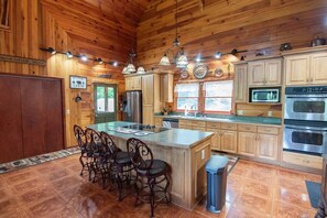 A cabin-style kitchen with wooden walls, a central island with chairs, stainless steel appliances, and a sign reading 'CABIN.' - Franklin, NC Cabin; Hot Tub; Mountain View; Starlink (Franklin)