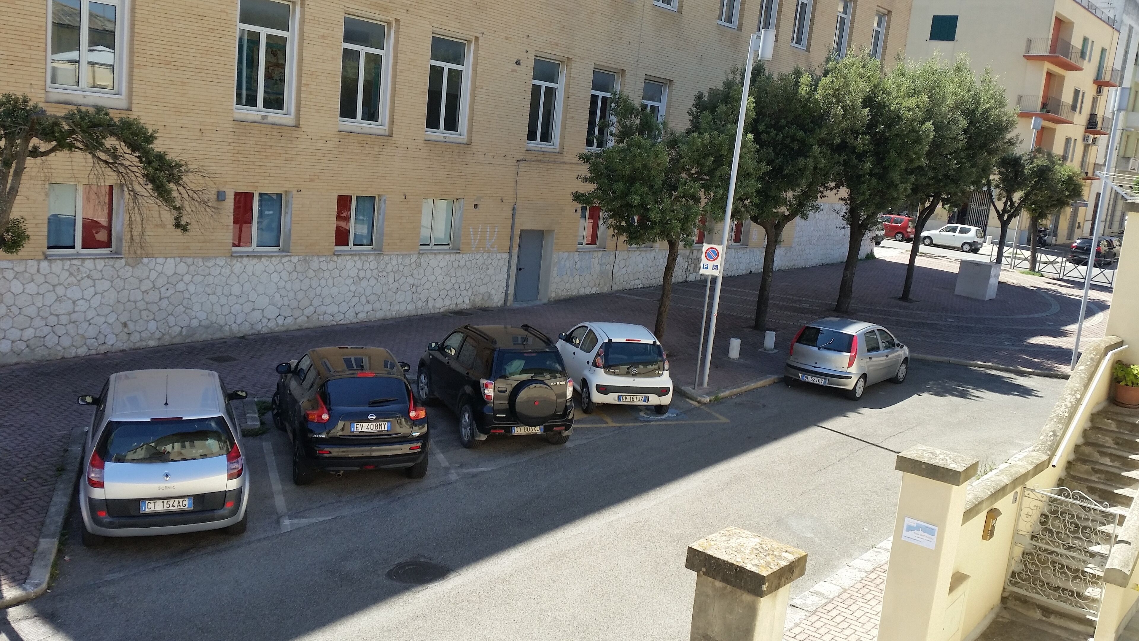 Un espace de stationnement où plusieurs voitures sont garées devant un immeuble doté de nombreuses fenêtres et de balcons.