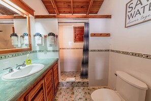 A bathroom with a wooden ceiling, a sink, a toilet, and a shower with a striped curtain.