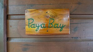 Une enseigne en bois portant l’inscription « Paya Bay », fixée à un mur en bois.