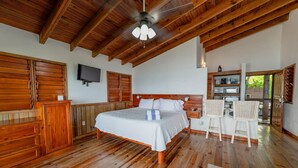 Une chambre avec un plafond en bois, un lit, une télévision et un coin cuisine.