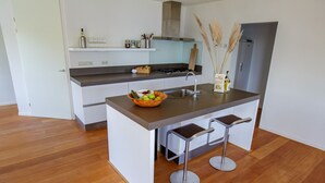 Une cuisine moderne dotée d’un îlot central, de deux tabourets de bar et d’une cuisinière intégrée.