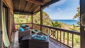 A covered outdoor seating area with wicker furniture and cushions, overlooking a beach. - Mangrove Suite - 2nd Floor Double (West End)