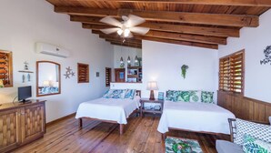 A room with two beds, wooden flooring, a ceiling fan, and a desk with a computer. - Mangrove Suite - 2nd Floor Double (West End)