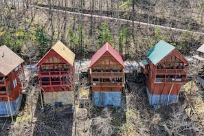 Tres cabañas con revestimiento de madera, una cabaña central con balcón y un bosque circundante.