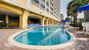 Un espace piscine d’hôtel avec une piscine à l’eau cristalline, des chaises longues et un bâtiment doté de balcons.