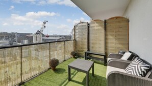 Uma varanda com grama sintética, mobiliário de vime e vista para a paisagem urbana.