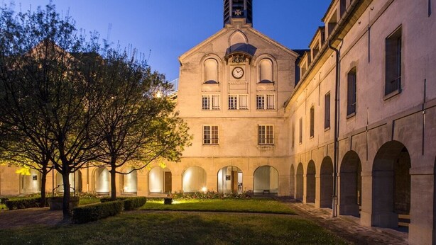 Um edifício histórico com uma torre do relógio, passagens em arco e um pátio bem iluminado.