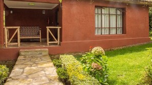 A rustic house with a thatched roof, a stone pathway leading to a wooden bench, and a small garden area with various plants. - Ingagi Lodge, UNIT 1, Single room (Kinigi,)
