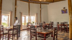 A spacious dining area with multiple tables and chairs, a thatched roof, and large windows allowing natural light. - Ingagi Lodge, UNIT 1, Single room (Kinigi,)